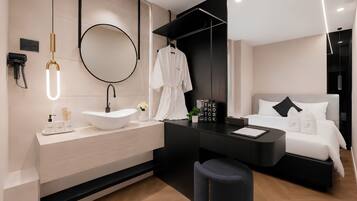 A modern hotel room with a large round mirror, a black vanity, a bed with white bedding, and a small seating area.
