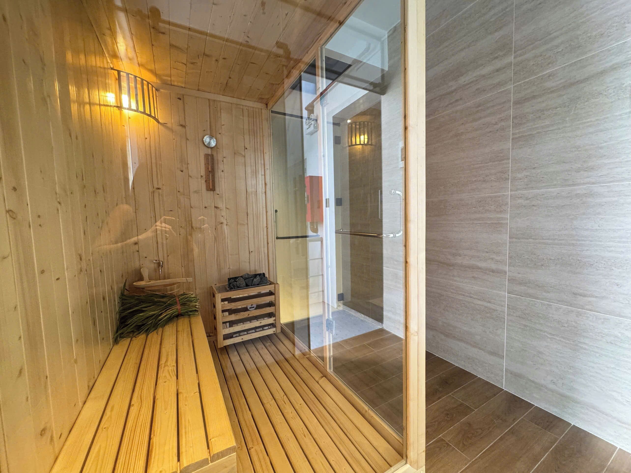 A wooden sauna room with a bench, a glass door leading to a shower area, and a wooden floor.