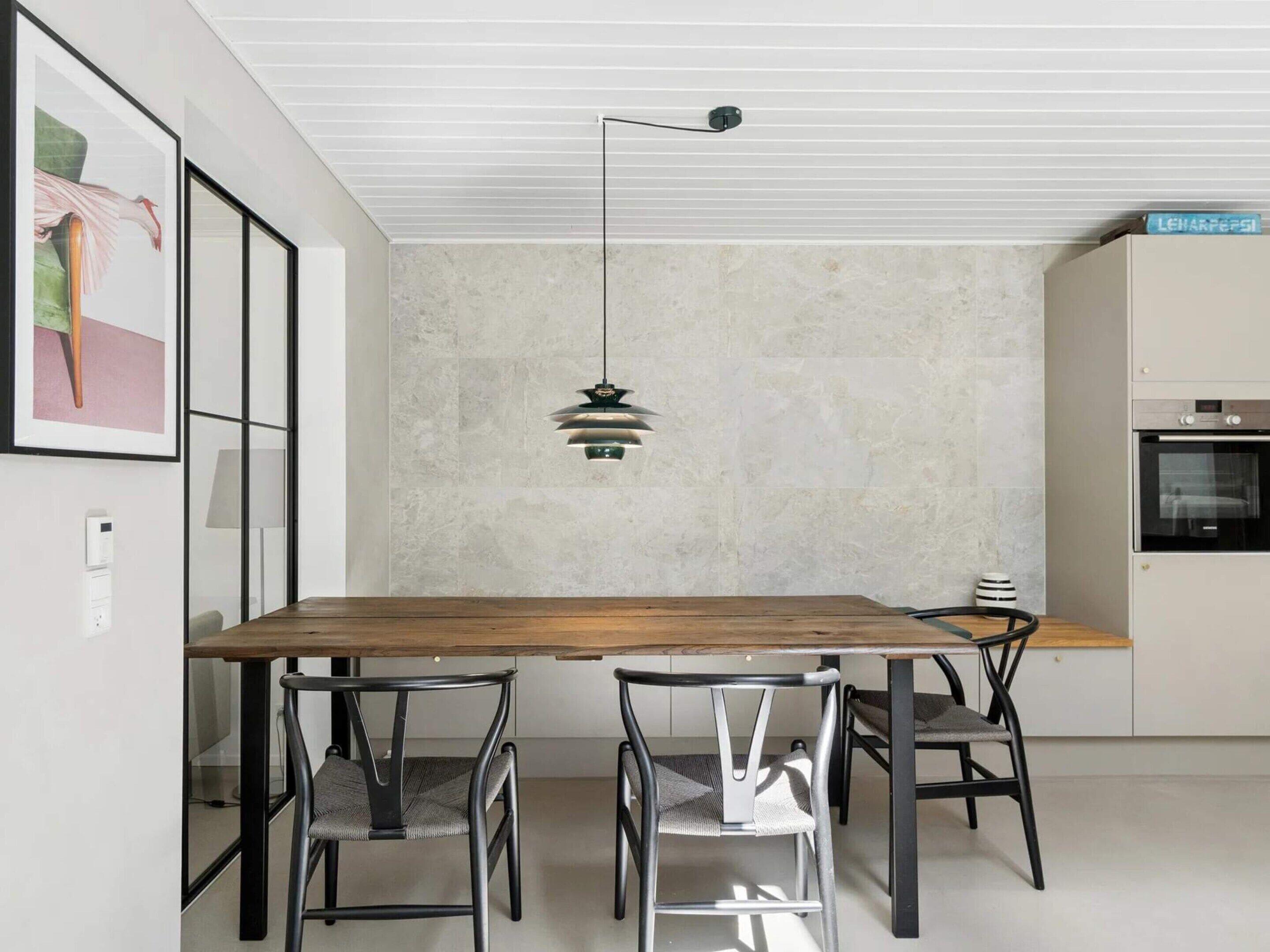 Un espace repas moderne avec une table en bois et des chaises en métal, un luminaire suspendu et une cuisine équipée d’un four.