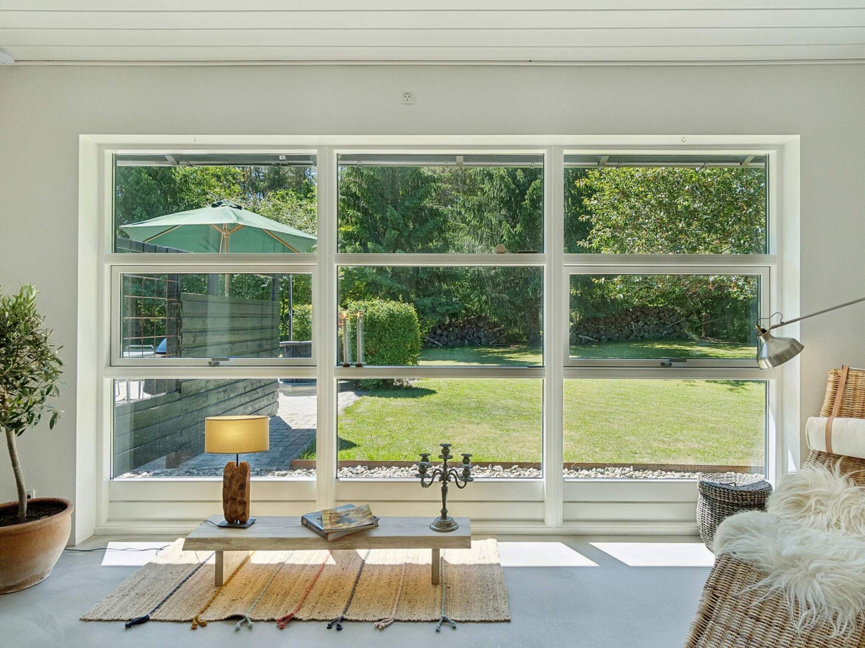 A room with a large window overlooking a garden, a bench with a lamp, and a potted plant.