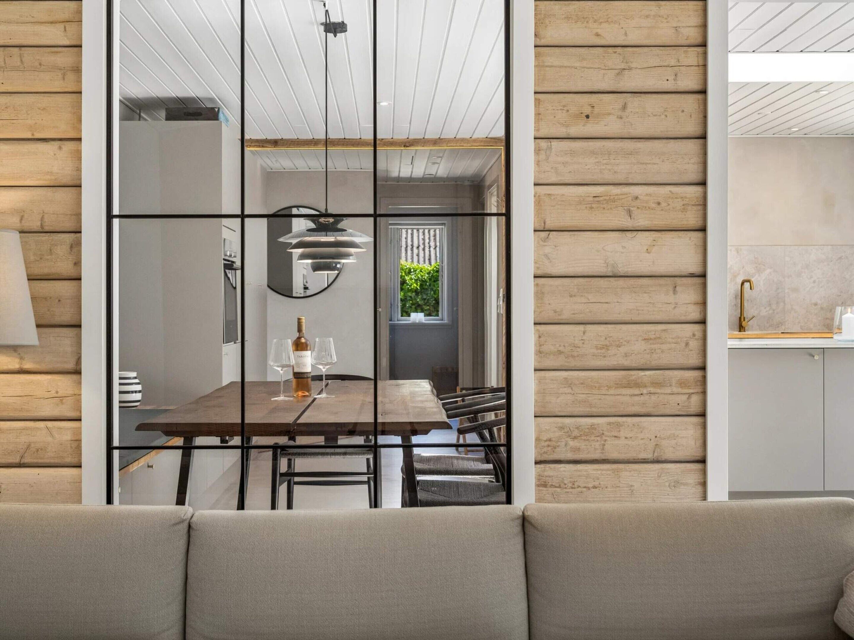A modern interior with a wooden wall, a dining area with a table and chairs, and a visible kitchen area.