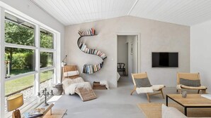 A spacious living room with a large window, a curved bookshelf, and a flat-screen TV mounted on the wall. - 4 Star Holiday Home in Ronde (Ronde)