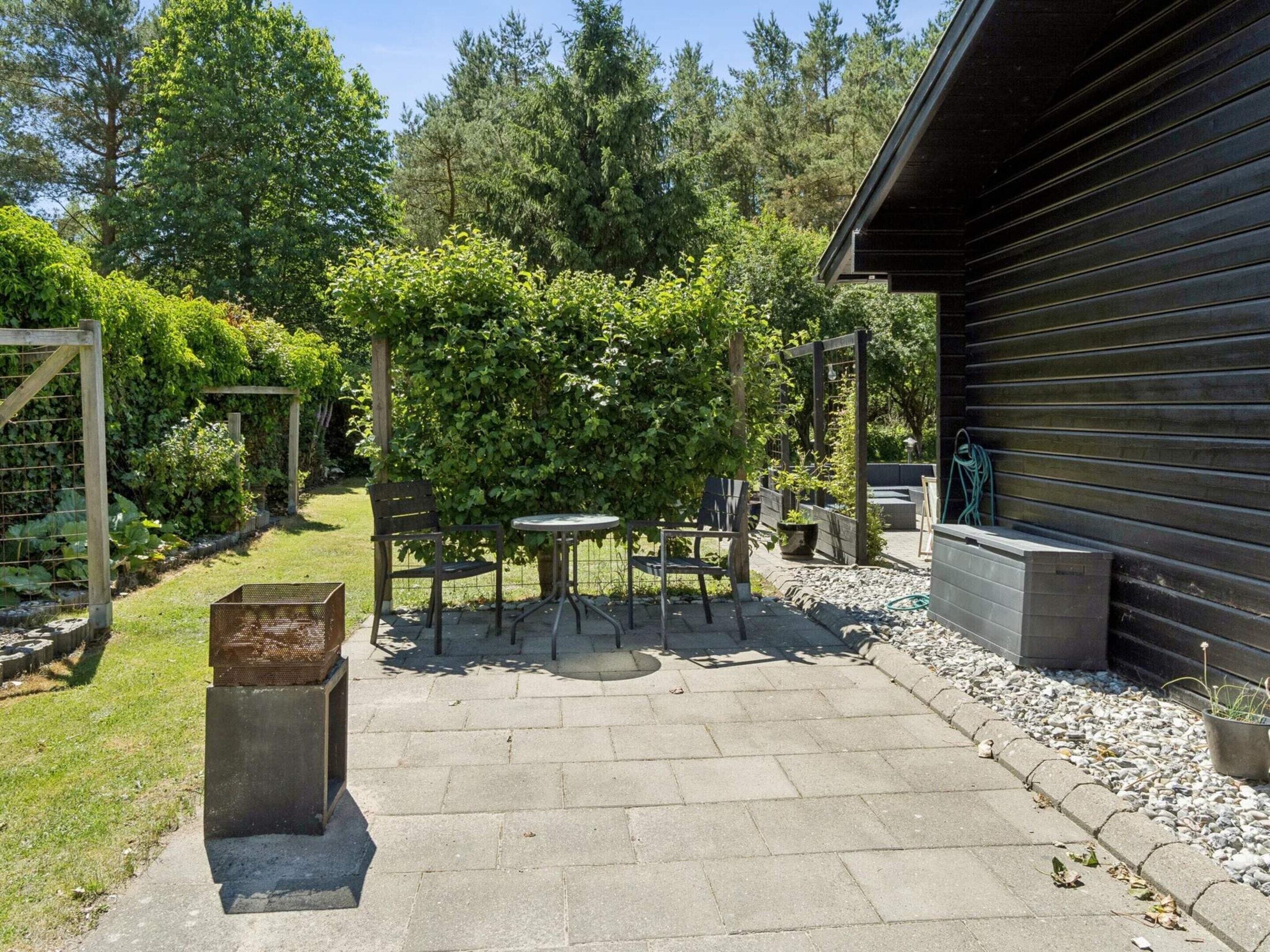 Un espace patio aménagé avec une table et des chaises, entouré de verdure et délimité par une clôture en bois.