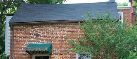 A brick house with a dark roof, a front door with a wreath, a small window, and a green awning.