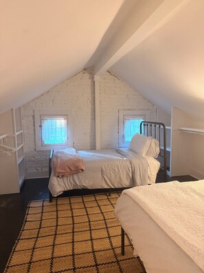 A bedroom with a sloped ceiling, two windows, a bed with a headboard, a bedside table, and a rug.