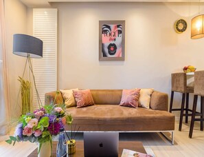 Un salon moderne avec un canapé, un ordinateur portable posé sur une table, une lampe sur pied et une horloge murale.