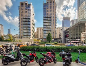 Une vue urbaine avec de hauts immeubles, un ciel dégagé et des scooters garés.