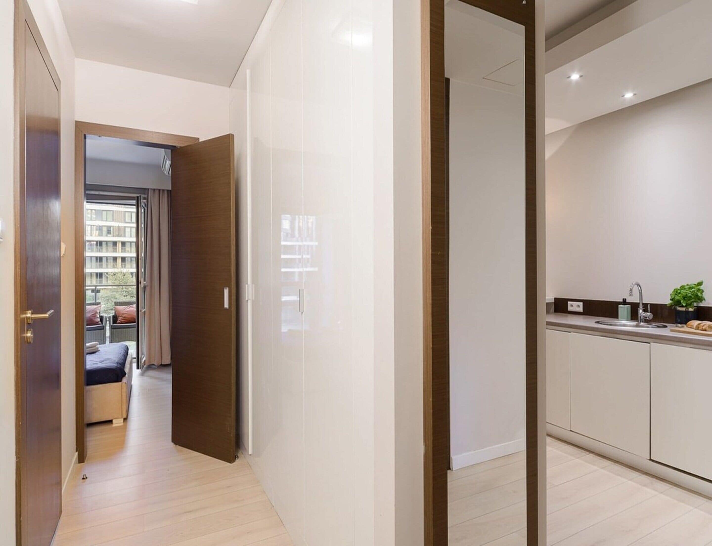 Une chambre d’hôtel moderne avec un plancher en bois, une vue sur le balcon extérieur et une kitchenette équipée d’un évier et d’un plan de travail.