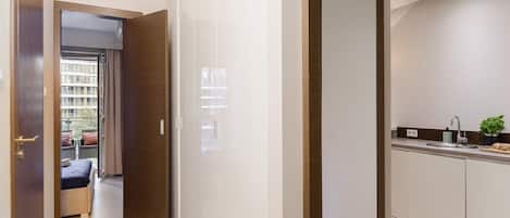 Habitación de hotel moderna con piso de madera, vista al balcón exterior y una kitchenette con lavamanos y encimera.
