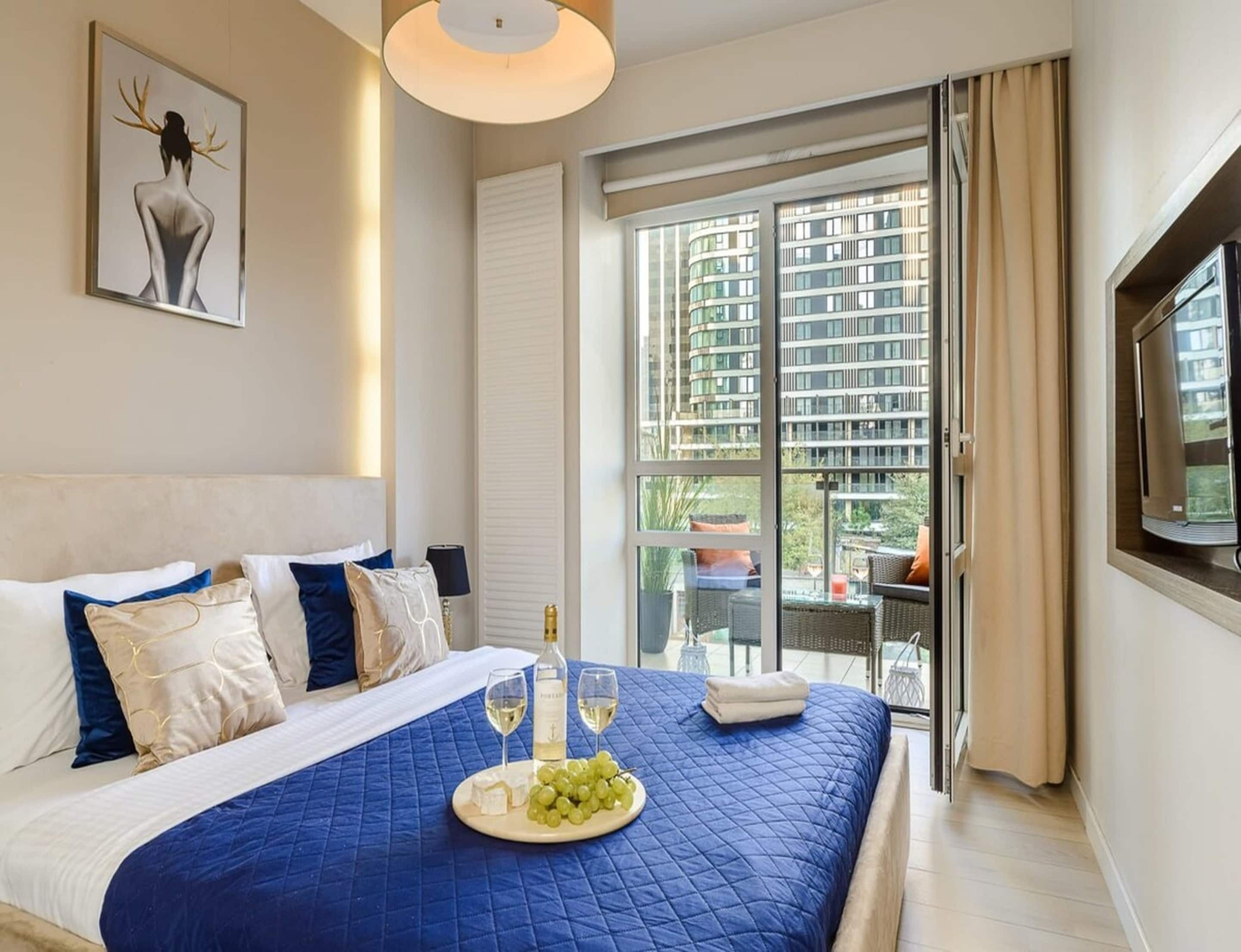 A hotel room with a large bed, a view of the city, and a balcony with outdoor furniture.