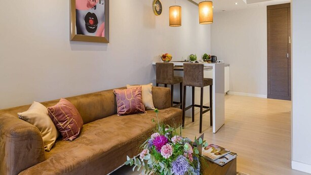 Ein modernes Wohnzimmer mit einer Couch, einem Couchtisch mit Blumen und einer Küchenzeile im Hintergrund.