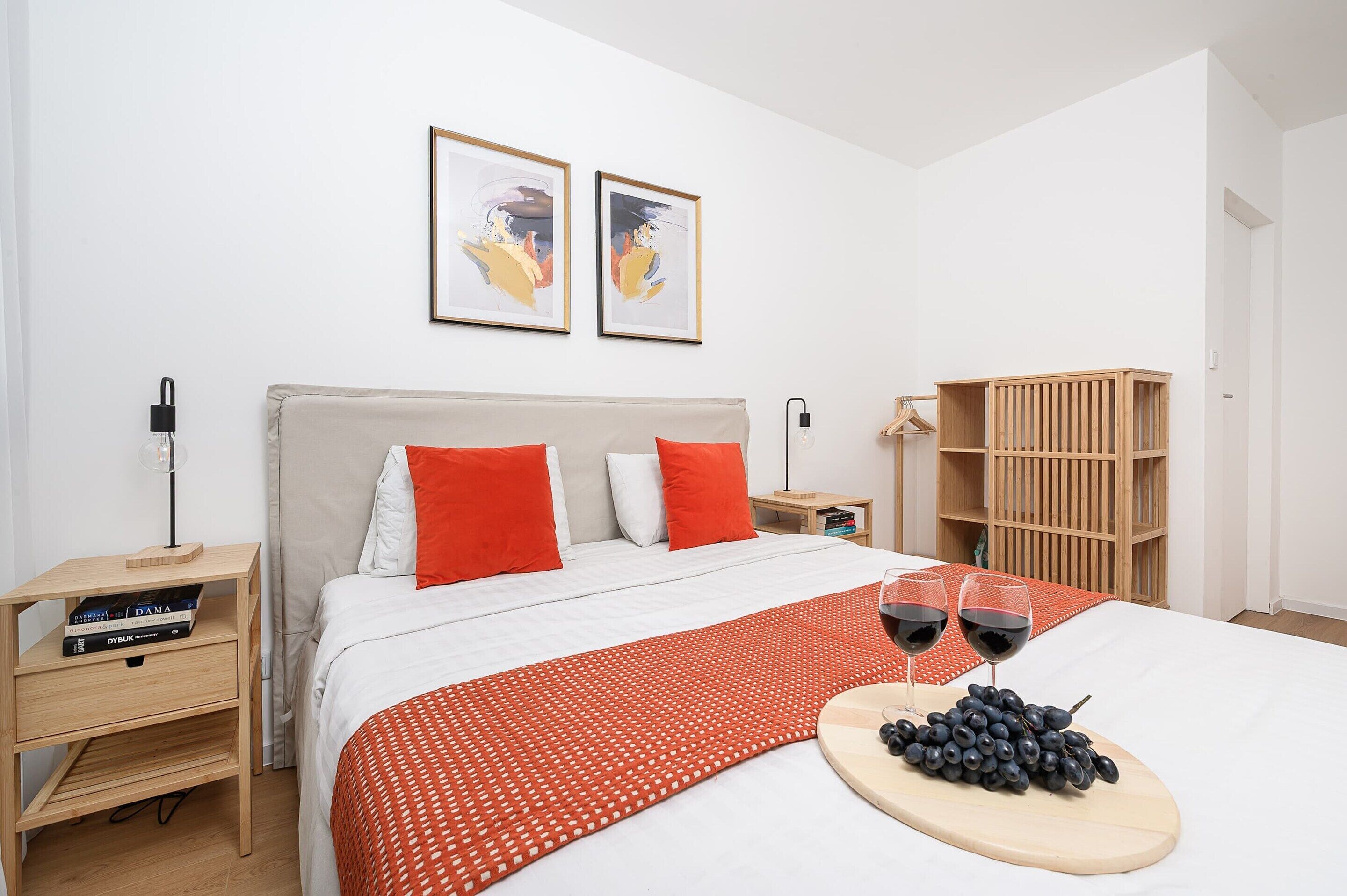 Een moderne slaapkamer met een bed, twee kussens, een nachtkastje, een houten kledingkast, en twee kunstwerken in lijsten aan de muur.