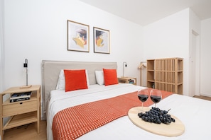 Un dormitorio moderno con cama, dos almohadas, una mesita de noche, un armario de madera y dos cuadros enmarcados en la pared.