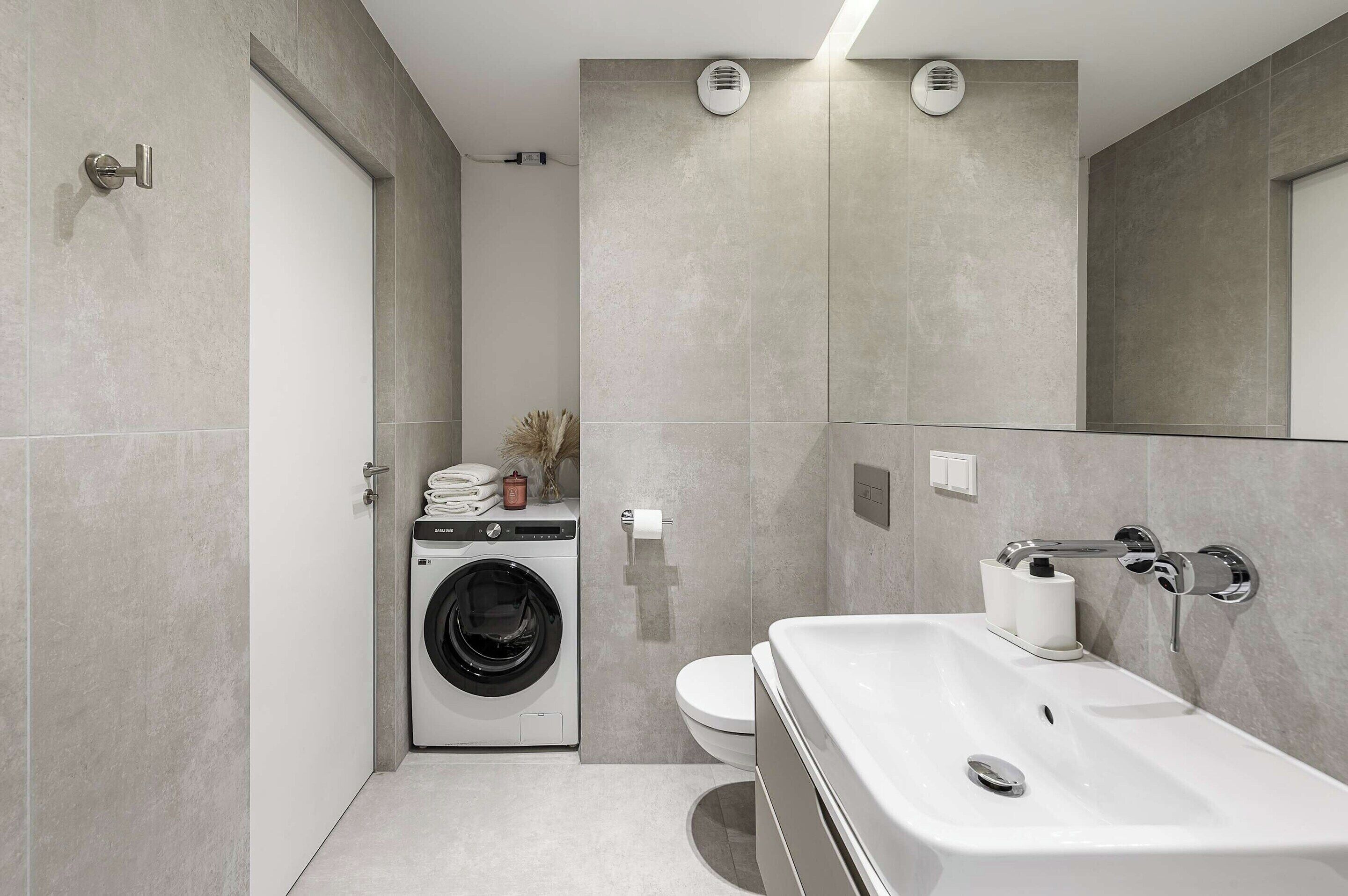Un baño moderno con lavadora integrada, inodoro y un lavamanos grande con espejo.