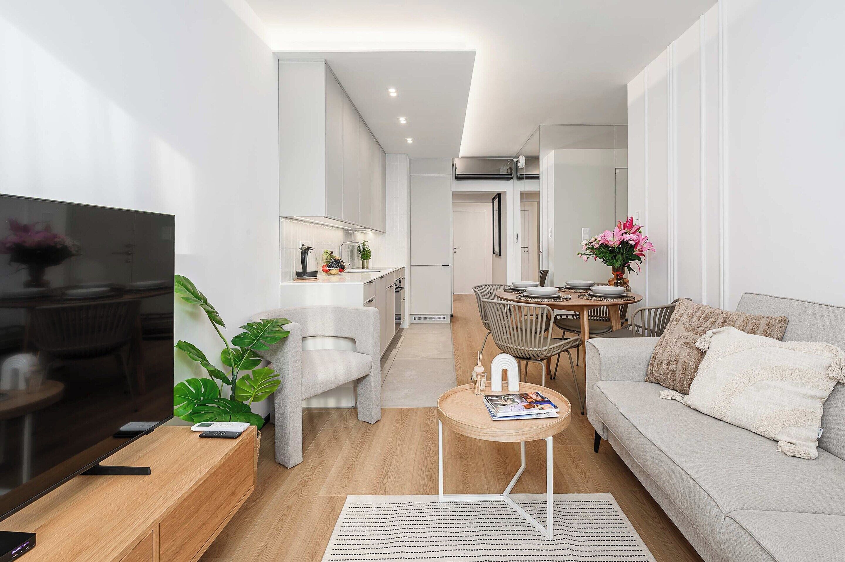 A modern living room with a sofa, coffee table, and a TV. There is a dining area with a table and chairs.