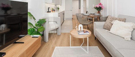 A modern living room with a sofa, coffee table, and a TV. There is a dining area with a table and chairs.