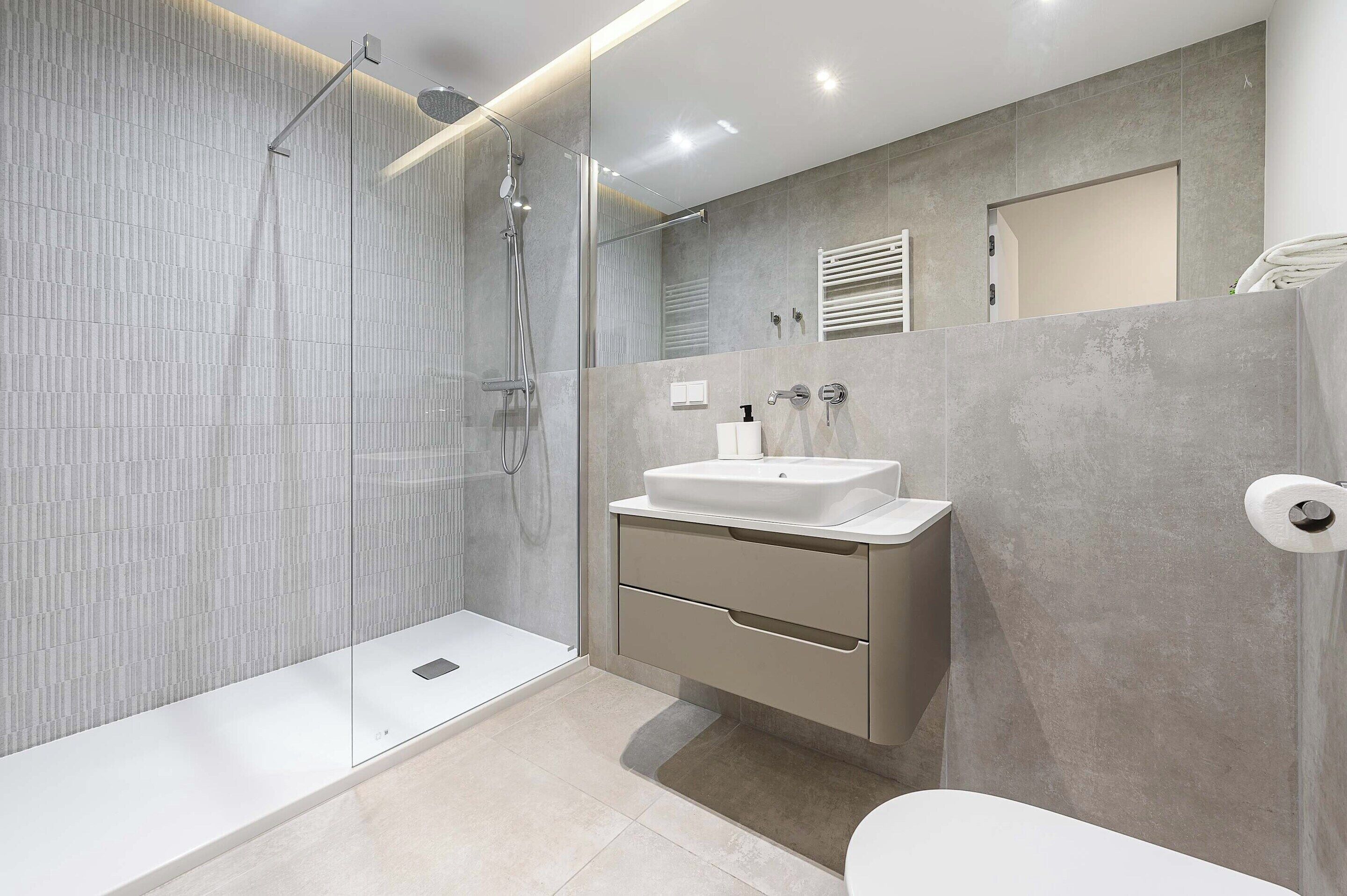 Un baño moderno con cabina de ducha de vidrio, lavabo blanco y retrete.