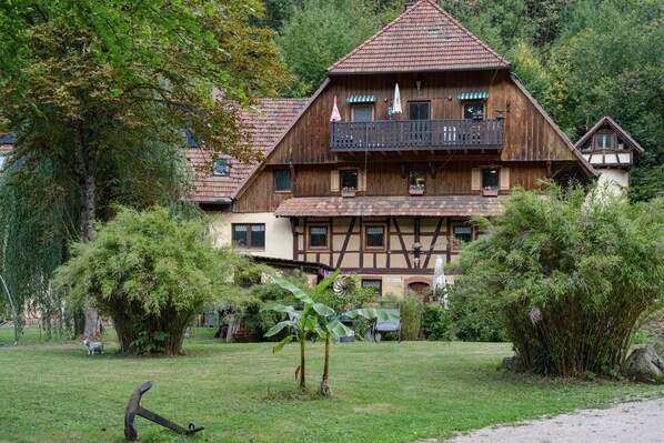 A traditional wooden house with a balcony, surrounded by lush greenery.