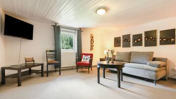 Ein Wohnzimmer mit einer Couch, zwei Sessel, einem Couchtisch, einem Fernseher und Kunstwerken an der Wand.