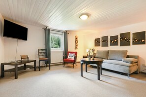 Een woonkamer met een bank, twee stoelen, een salontafel, een televisie en kunst aan de muur.