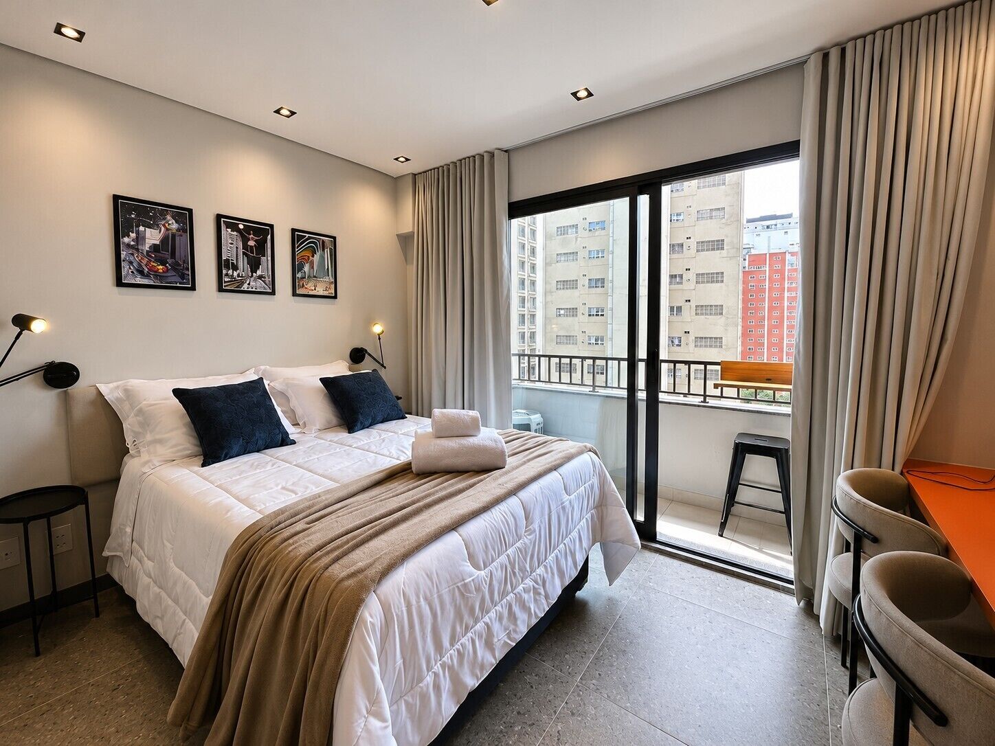 Een hotelkamer met een bed, een bureau, een stoel, een balkon en uitzicht op de stad.