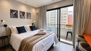 Une chambre d’hôtel avec un lit, un bureau, une chaise, un balcon et une vue sur la ville.