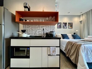 Une chambre d’hôtel moderne dotée d’une kitchenette, d’un lit avec vue et d’œuvres d’art accrochées au mur.