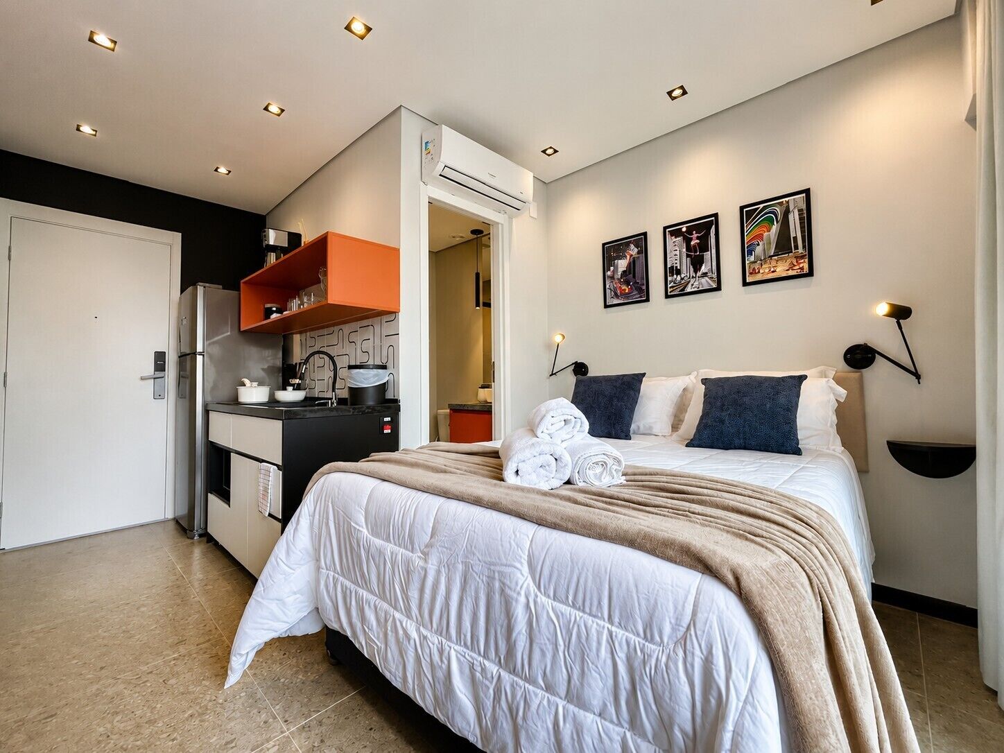 A modern hotel room with a bed, a kitchenette, and a bathroom.