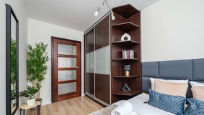 Een slaapkamer met een bed, nachtkastje, spiegel, kledingkast en een potplant.