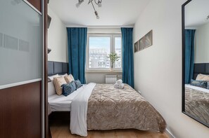 A bedroom with a bed, a window with curtains, a radiator, and a mirror. - Warsaw Flat Near Old Town (Warsaw)