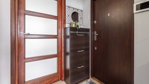 Een kamer met een houten deur, een donkere houten kast met lades en een kleine spiegel aan de muur.