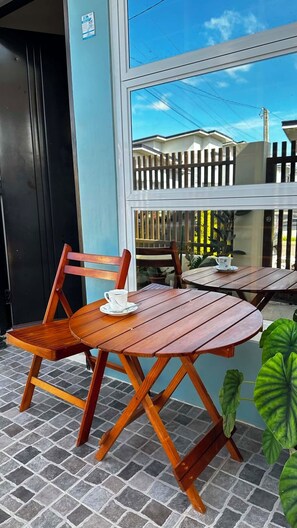 A wooden table and chair set on a tiled floor, with a window overlooking a fenced area.