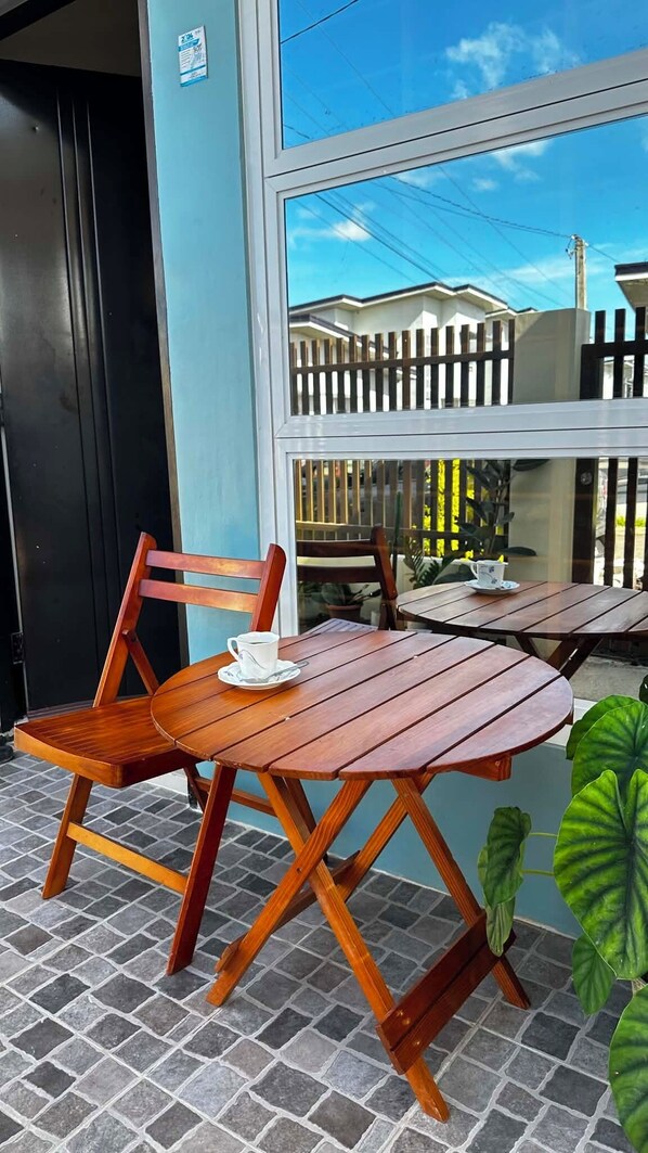A wooden table and chair set on a tiled floor, with a window overlooking a fenced area.