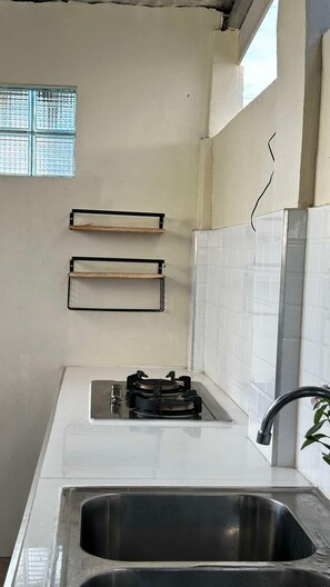 A kitchen with a gas stove, two shelves, a sink, and a window with blinds.