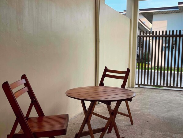 A small outdoor seating area with two wooden chairs and a table, adjacent to a building with a white exterior and a metal gate.