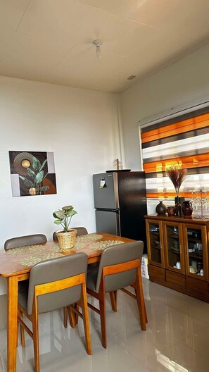 A dining area with a table and chairs, a refrigerator, a cabinet with glass doors, and a wall-mounted light fixture.