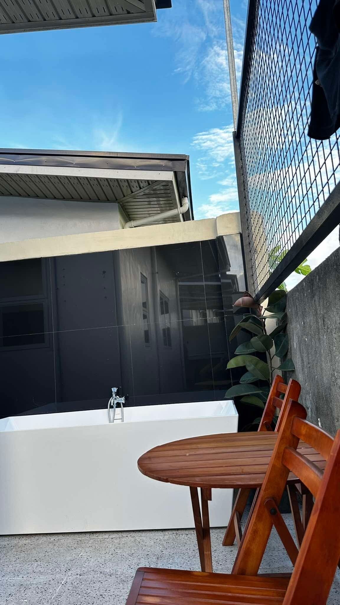 A modern outdoor bathroom with a white tub, a table, and chairs.
