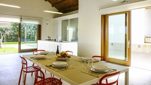 A dining area with a table set for four, a kitchen in the background, and a view of a garden through a glass door. - Villa in Sicily With Pool Near Erice & Trapani (Marsala)