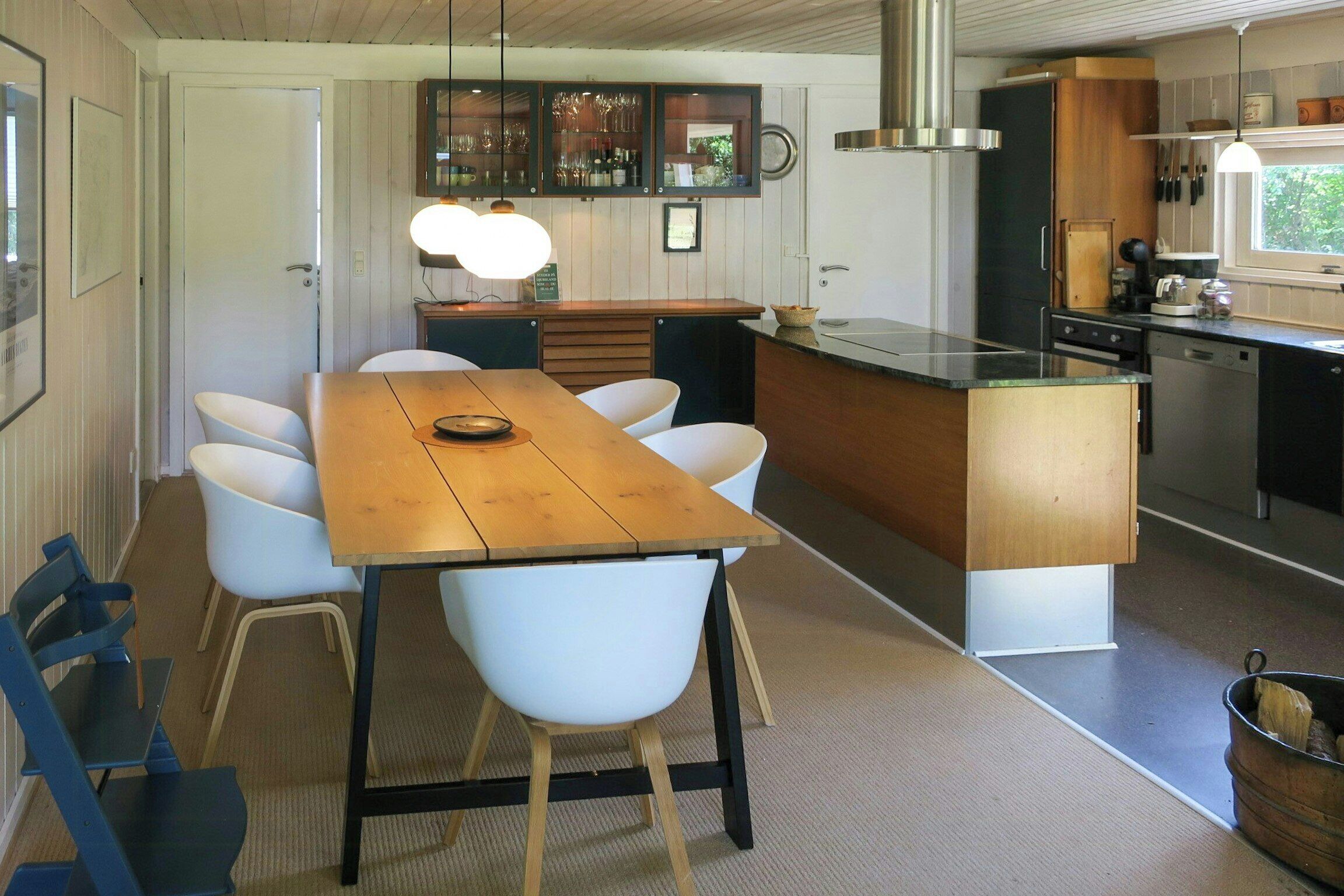 Une cuisine moderne avec un îlot central, des chaises blanches et une table à manger en bois.