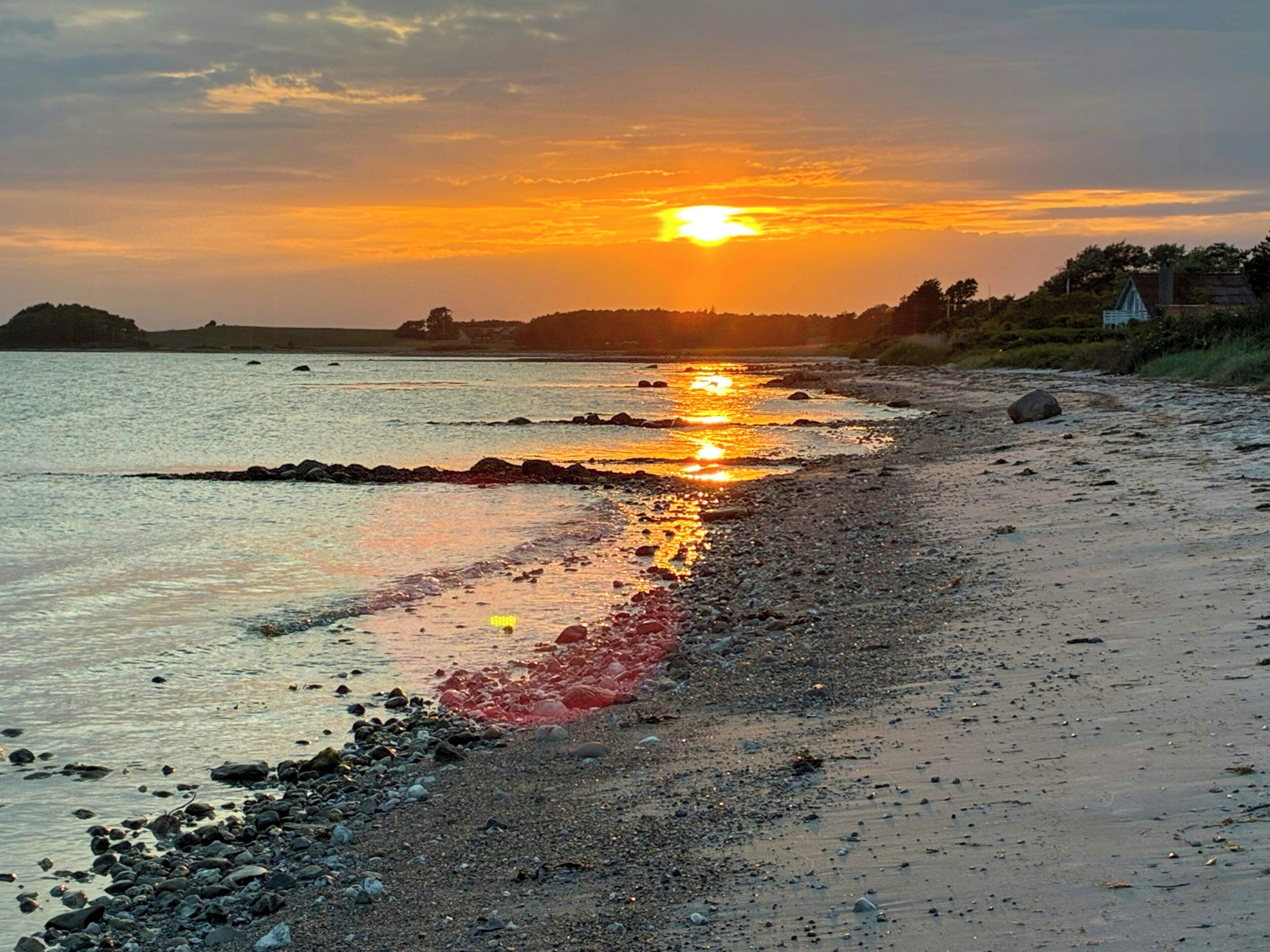 Ein Strand bei Sonnenuntergang, ruhiges Wasser und eine felsige Küste.