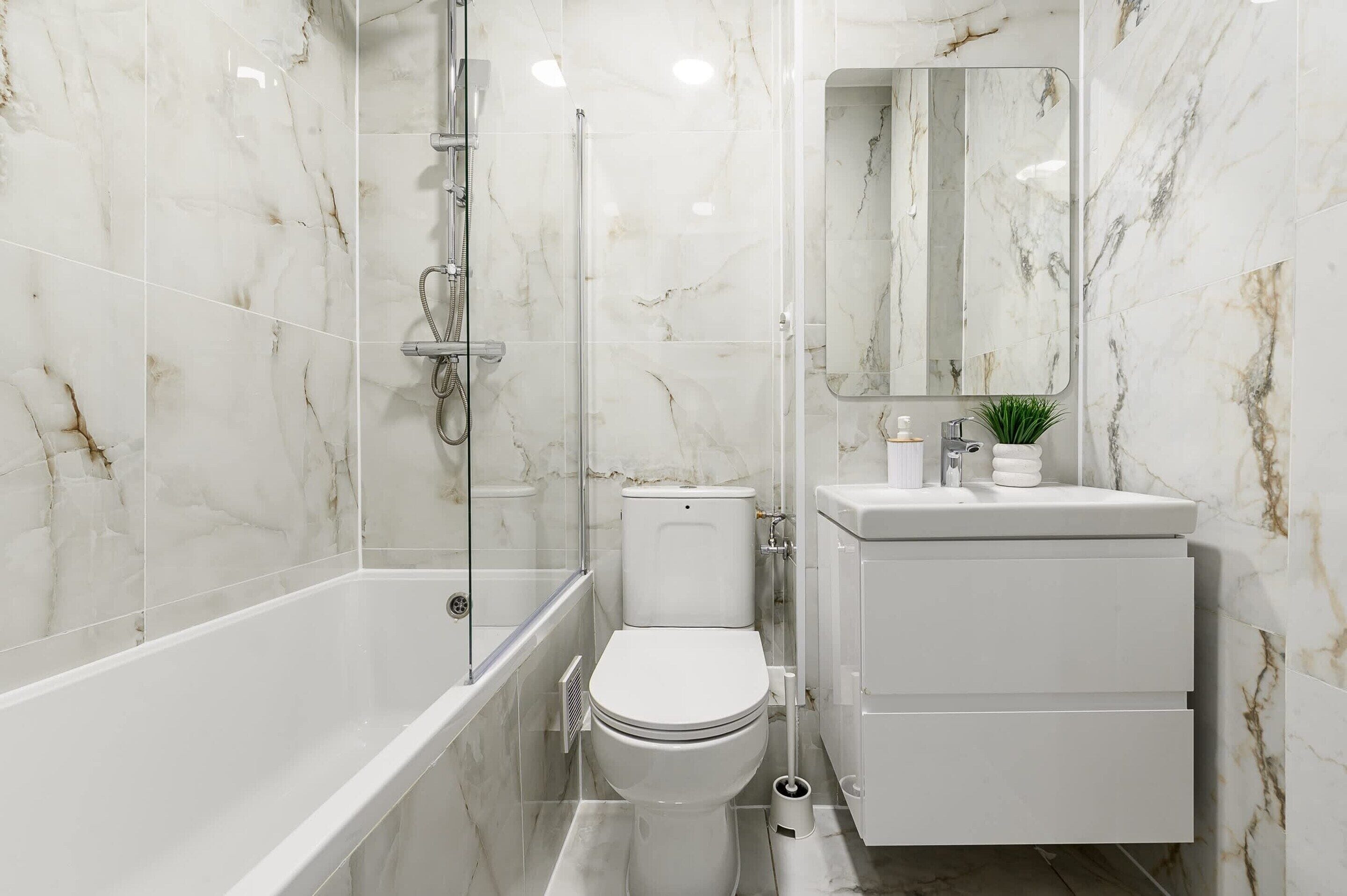 Un baño con ducha de vidrio, inodoro y lavamanos con espejo.