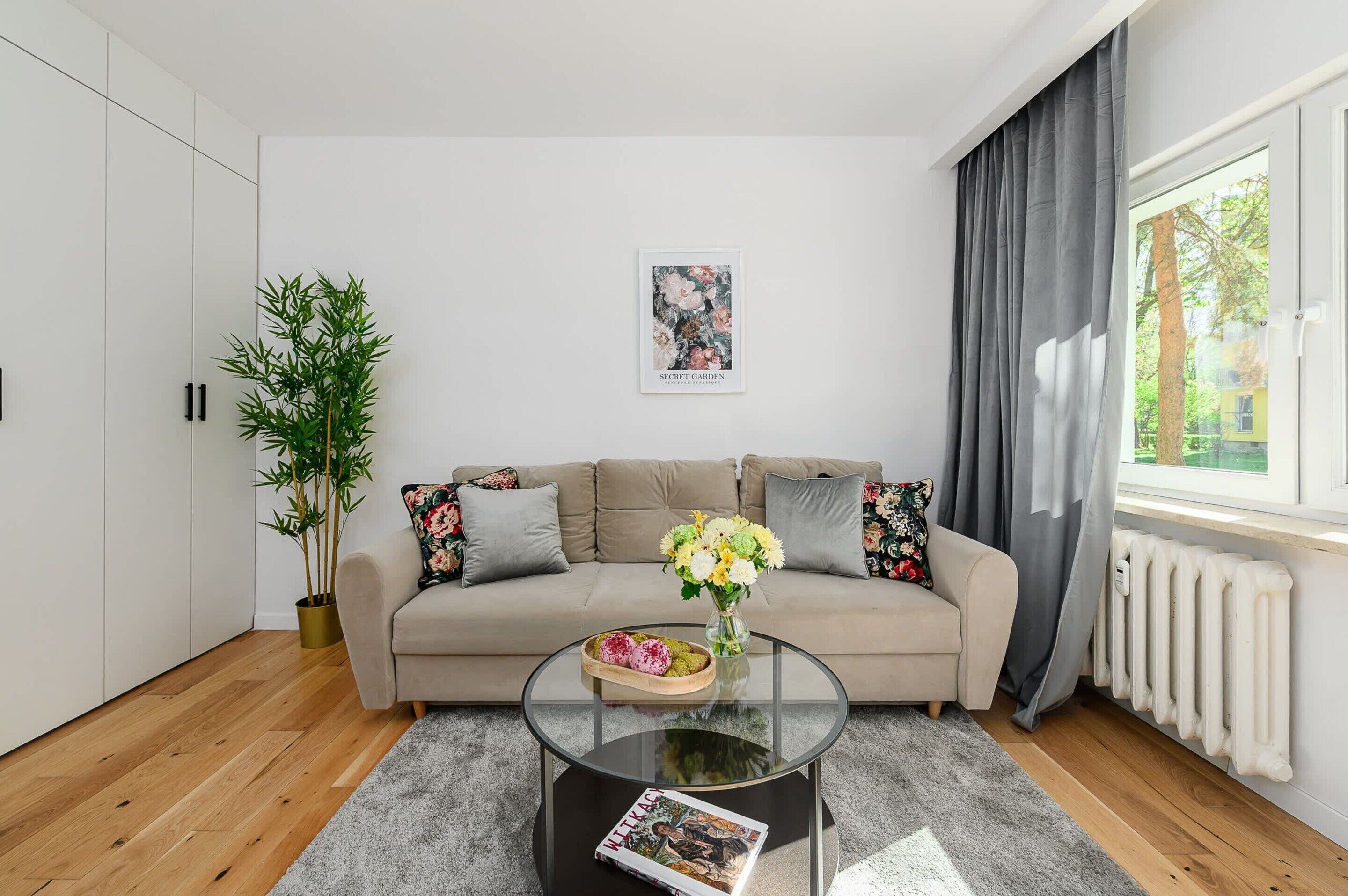 A modern living room with a sofa, a glass coffee table, a potted plant, and a poster on the wall.
