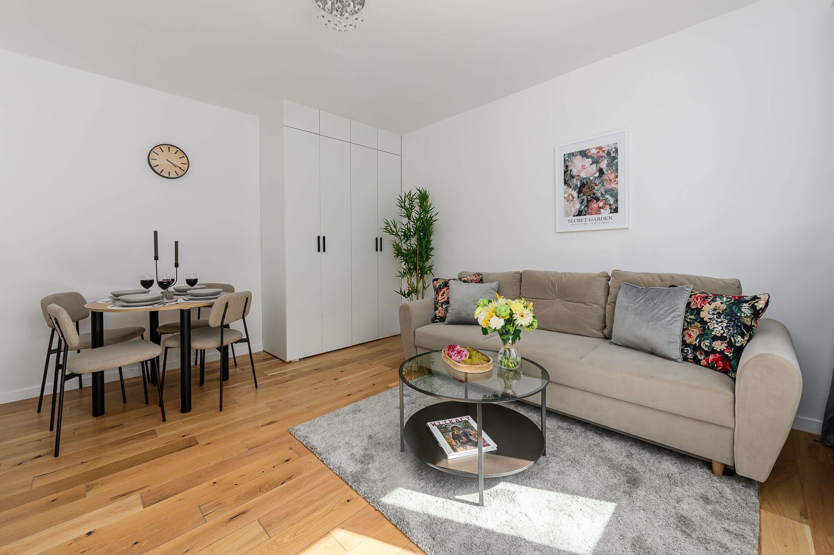 A modern living room with a sofa, coffee table, dining table, chairs, and a clock on the wall.