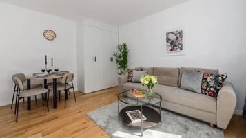 A modern living room with a sofa, coffee table, dining table, chairs, and a clock on the wall.