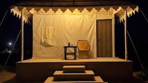 A tent with a covered seating area, steps leading up to it, and a small table with a chair. - Marawi Desert Resort-Luxury Swiss Tents in Jaisalmer (Sam)