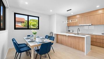 A modern kitchen with wooden cabinets, a white countertop, and a dining area with blue chairs and a table set for four.