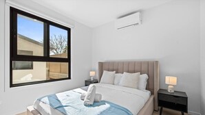 Ein Schlafzimmer mit einem Bett, zwei Nachttischen, einem Fenster und einer Klimaanlage.