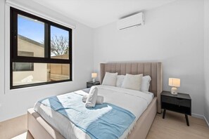 A bedroom with a bed, two bedside tables, a window, and an air conditioning unit. - Modern 4BR Retreat Near Brisbane CBD (Eight Mile Plains)