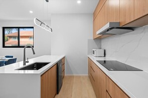 A modern kitchen with a built-in dishwasher, a microwave, and a black induction cooktop. - Modern 4BR Retreat Near Brisbane CBD (Eight Mile Plains)