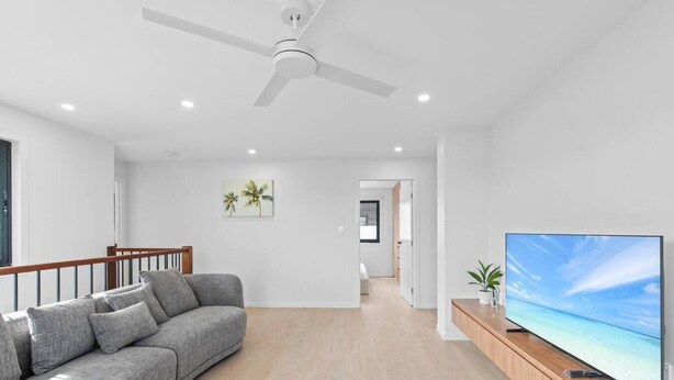 Ein modernes Wohnzimmer mit einem grauen Sofa, einem Flachbildfernseher auf einem Holzboden und einem Deckenventilator.